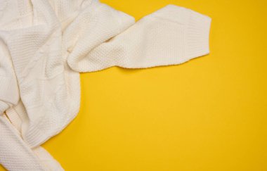 Sağ üst köşede, sarı arka planda beyaz örülü bir süveterin kenarı. Sıcaklık, kış ve moda kavramı. Boşluğu kopyala