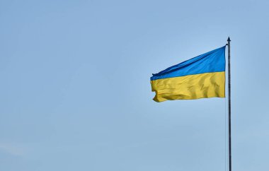 Yüksek bir bayrak direğinde Ukrayna bayrağı, açık mavi gökyüzünde dalgalanan mavi ve sarı bayrak.