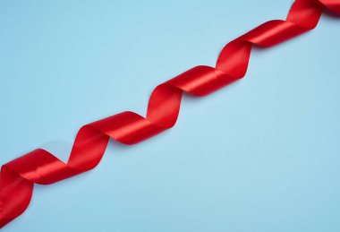 Kırmızı saten bir kurdele spiral şeklinde bükülür ve mavi bir arkaplanda köşegen şeklinde yerleştirilir.