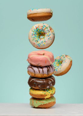 Çeşitli dolguları ve jöleleri olan bir yığın donut, birkaç tane de yukarı doğru yükselen. Mavi arkaplan.