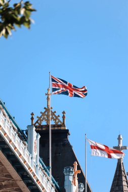 Londra, İngiltere - 11 Ağustos 2022: Yazın Tower Bridge 'in üzerinde dalgalanan Union Jack ve St George Cross bayraklarının yakın çekimi