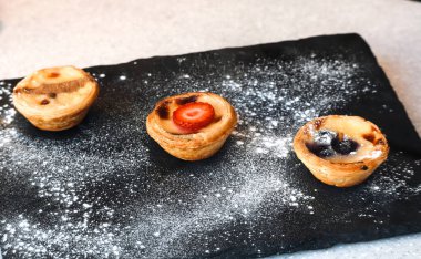 Portekiz pastası de nata tatlısı pudra şekeri tozlu, siyah bir tahtada servis edilir..