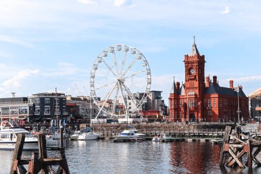 Cardiff, Wales - 14 Ağustos 2022: Dönme dolap ve Cardiff Körfezi 'ndeki tarihi kırmızı Pierhead Binası güneşli bir öğleden sonra yat limanında teknelerle