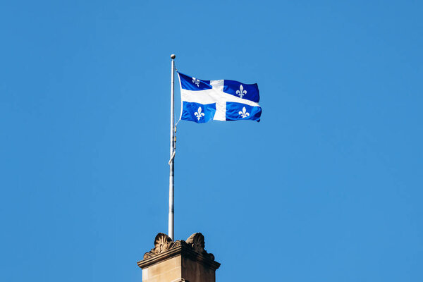 Монреаль, Канада - 11 августа 2025 года: флаг Квебека машет на вершине исторического здания в центре Монреаля против ясного голубого неба