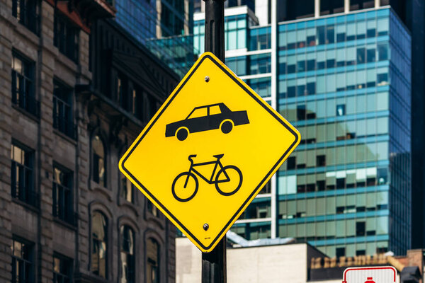 Монреаль, Канада - 11 августа 2025 года: Желтый дорожный знак, показывающий символы автомобилей и велосипедов в центре Монреаля с современными стеклянными зданиями на заднем плане