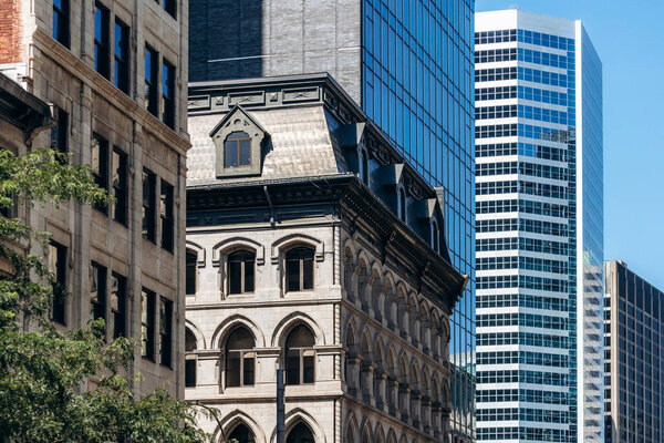 Монреаль, Канада - 11 августа 2025 года: Историческое каменное здание с арочными окнами, окруженное современными стеклянными небоскребами в центре Монреаля