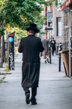 Montreal, Kanada - 12 Ağustos 2025: Geleneksel ortodoks Yahudi kıyafetleri içindeki bir adam Montreal 'in Mile End Yahudi mahallesinde bir cadde boyunca yürüyor.