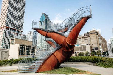 Montreal, Kanada - 14 Ağustos 2025: Montreal şehir merkezinin modern siluetine karşı kurulu paslı çelik yapılar ve yükseltilmiş yürüyüş yolları ile çarpıcı bir kamu sanatı tesisi