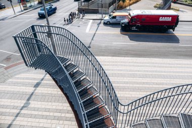 Montreal, Kanada - 14 Ağustos 2025: Yoğun bir şehir caddesine bakan modern bir heykel merdiven yapısı ve aşağıdan geçen bir grup yayanın yüksek açılı görüntüsü