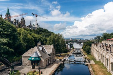 Ottawa, Kanada - 13 Ağustos 2025: Taştan binalar, patikalar ve Ottawa Nehri boyunca yürüyen insanlarla dolu Rideau Kanalı 'nın geniş görüşü