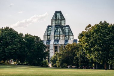 Ottawa, Kanada - 13 Ağustos 2025: Güneşli bir yaz gününde Ottawa şehir merkezinde yeşil bir çimenlik ve ağaçların üzerinde yükselen Kanada Ulusal Galerisi manzarası.