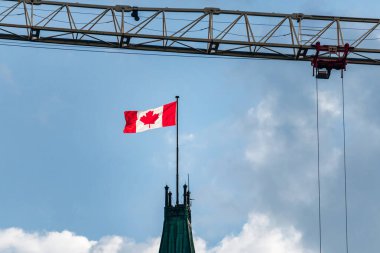 Parliament Hill 'deki Barış Kulesi' nin üzerinde Kanada bayrağı dalgalanırken arka planda bir inşaat vinci görülüyor.