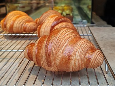 Bir fırın rafında sergilenen taze altın kruvasanlar, tuhaf katmanlar, parlak kabuk ve Nice 'teki bir dükkanın vitrininde geleneksel Fransız hamur işi işçiliği.