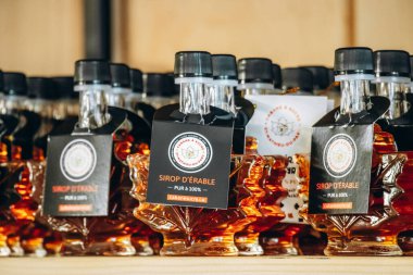 Saint-Mathieu-du-Parc, Kanada - 16 Ağustos 2025: Geleneksel bir şeker deposunda sergilenen akçaağaç yapraklı cam kaplarda saf Quebec akçaağaç pekmezi şişeleri