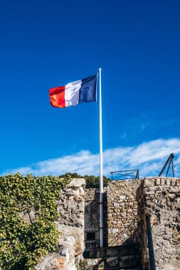 Grimaldi Kalesi 'nin taş duvarları üzerinde mavi gökyüzüne karşı dalgalanan Fransız ulusal bayrağı