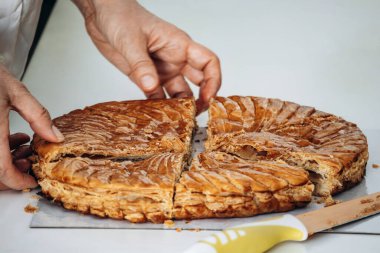 Galette des Rois dilimlerini kestikten sonra ayıran bir kadın, geleneksel olarak Ocak ayındaki Epifani kutlamalarında paylaşılan gevrek poğaça ve badem frangipanından yapılan Fransız tatlısıdır.