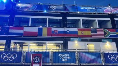 Livigno, İtalya - 6 Şubat 2026: Milano Cortina 2026 Uluslararası bayrak, bayrak ve karlı Alpler ile Olimpiyat tribünleri Livigno, İtalya 'da alacakaranlıkta