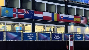 Livigno, İtalya - 6 Şubat 2026: Milano Cortina 2026 Uluslararası bayrak, bayrak ve karlı Alpler ile Olimpiyat tribünleri Livigno, İtalya 'da alacakaranlıkta