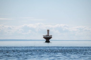 Açık deniz feneri kulesi Baie Sainte Catherine yakınlarındaki St. Lawrence Nehri 'nin sakin sularında ufukta yumuşak bulutlar görünen geniş mavi gökyüzünün altında duruyor.