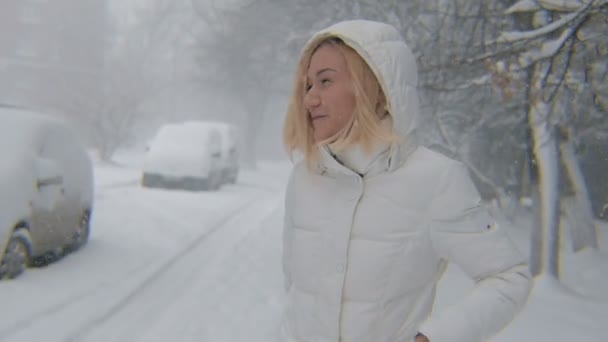 Menina loira jovem andando sorrindo na neve no dia de inverno — Vídeo de Stock