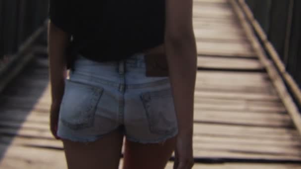 Ragazza in jeans corti che cammina sul ponte di legno in estate — Video Stock