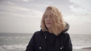 Sahilde güneşin tadını çıkarma ve rüzgarda gülümseyen genç sarışın kız