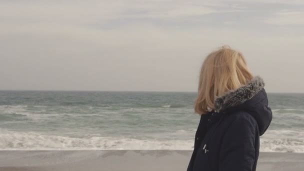 Joven rubia camina por la playa y sonríe al viento — Vídeo de stock