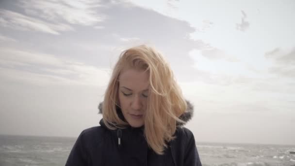 Jong blond meisje koesteren in de zon op het strand en lachend in de wind — Stockvideo