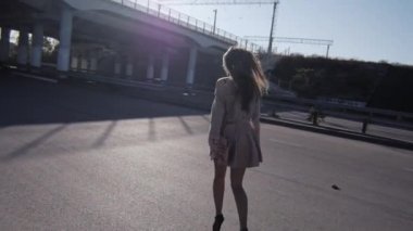 Kadın asfaltta köprünün altından kameradan günbatımında uzaklaşır