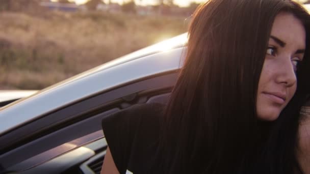 Молодая девушка смотрит и позирует возле машины на закате — стоковое видео