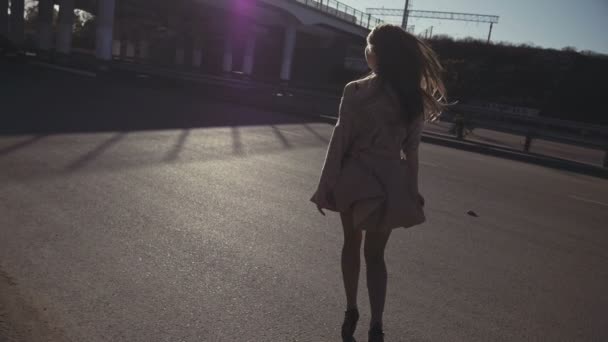 Mulher se afasta no asfalto da câmera sob a ponte ao pôr do sol — Vídeo de Stock