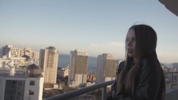 Blonde vrouw roken koesteren in de deken op hoge verdieping bij gebouwen achtergrond — Stockvideo