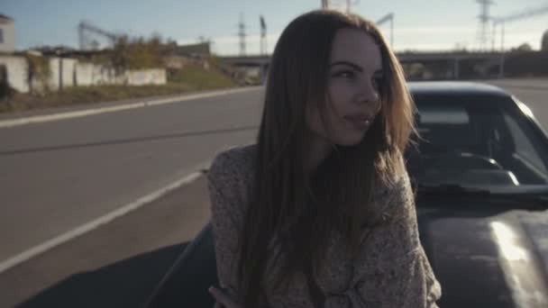 Mujer rubia tímida mirando a la cámara, mirando hacia abajo sentado en la capucha del coche — Vídeos de Stock