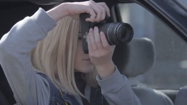 Ragazza bionda scattare foto dalla finestra con fotocamera professionale in auto vecchia — Video Stock