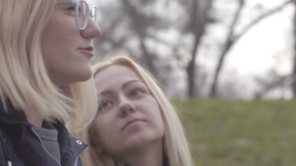 Duas meninas sentadas no banco no parque da cidade e falando — Vídeo de Stock