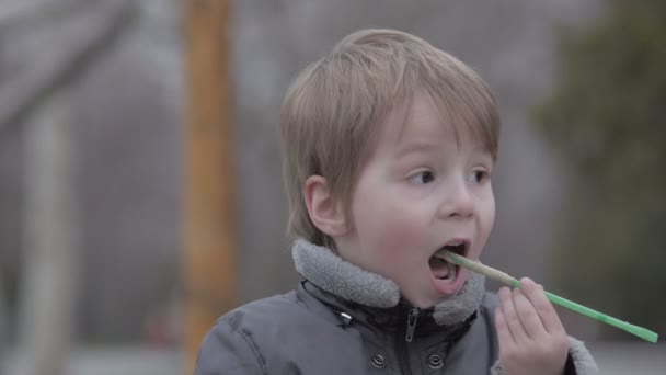 Kleiner Junge trinkt Kakao aus Tubuli im Park und saugt Getränk aus Plastikbecher — Stockvideo