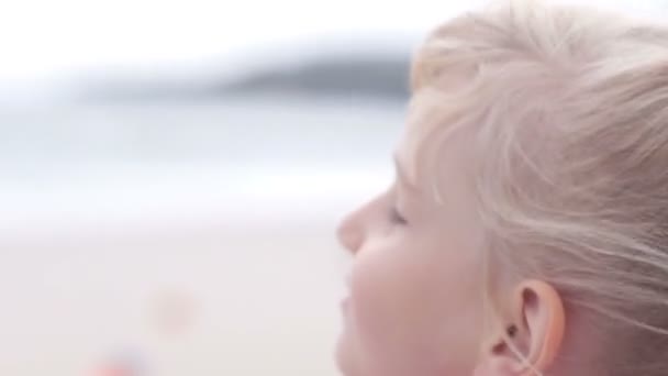 Junges blondes Mädchen träumt am Meer, lächelt und blickt zurück — Stockvideo