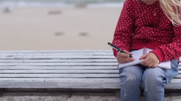 Маленька дівчинка пише в блокноті біля моря — стокове відео