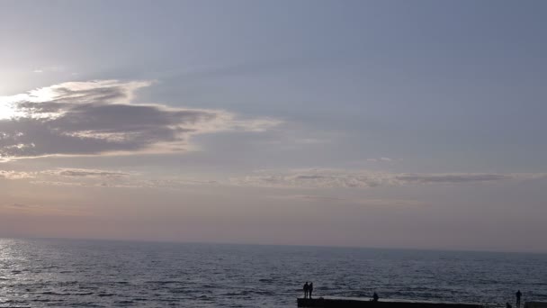 Salida del sol en la playa donde el sol se oculta de las nubes y el pescador en el muelle — Vídeo de stock