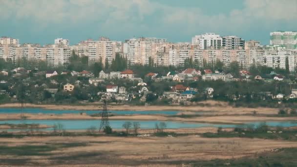 Masten der alten Elektrizität auf Feldern und ein See mit Gebäuden im Hintergrund — Stockvideo