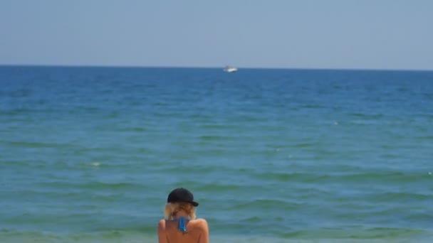 Chica Relajarse en la playa y ver el barco en catamarán en el mar en el fondo — Vídeo de stock