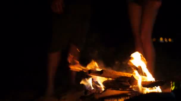 Vreugdevuur branden op een strand met benen van de mensen op de achtergrond sluiten — Stockvideo