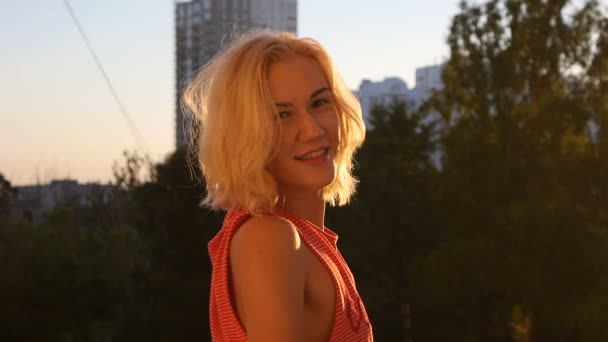 Félénk szőke lány pillantást a nyári naplemente mosolyogva lassítva — Stock videók