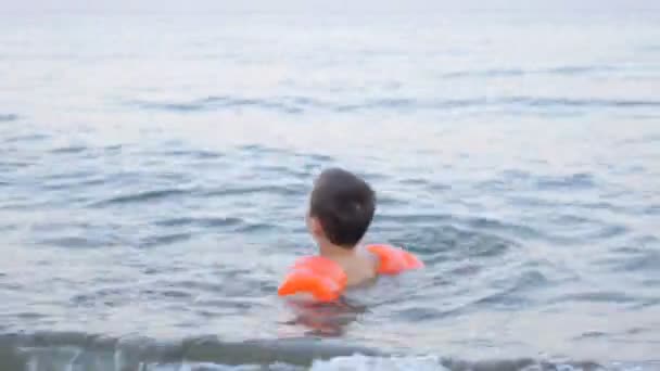 Niño jugando en olas en la playa en brazaletes inflables en Crepúsculo — Vídeos de Stock