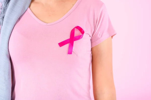 Muslim woman wearing a hijab with a ribbon on her chest shows prevention of breast cancer. On a pink backdrop, breast cancer concept, cancer prevention concept.