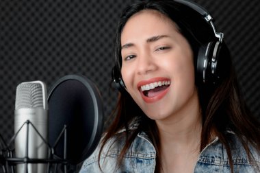 Müzik ve mikrofona tutkusu olan Asyalı kadın şarkıcı. Profesyonel bir stüdyoda şarkı söylerken. Müzik konsepti, ses kaydı konsepti.