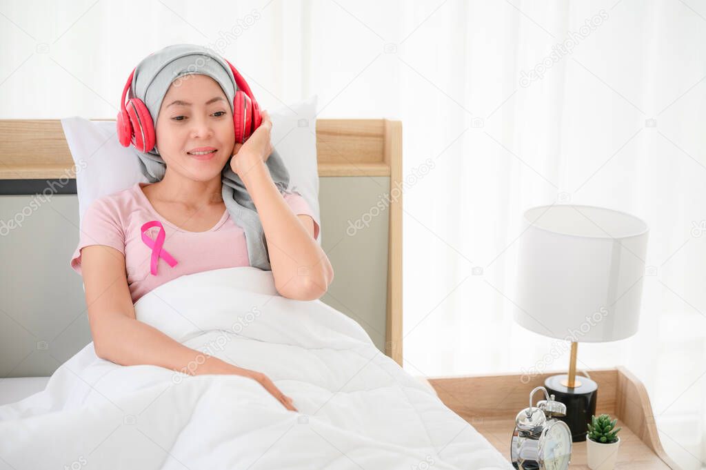 Young asian women wearing hijab Sit on the smartphone in the bed and put on the headphones. Represents recovery from a breast cancer illness. breast cancer concept, cancer prevention concept.