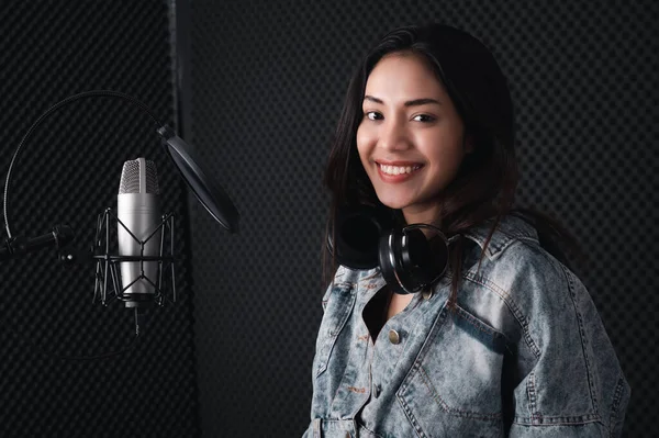 Asian female singer with a passion for music and microphone. While playing her guitar in a professional studio. Music concept, sound recording concept.