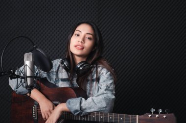 Müzik ve mikrofona tutkusu olan Asyalı kadın şarkıcı. Profesyonel bir stüdyoda gitar çalarken. Müzik konsepti, ses kaydı konsepti.