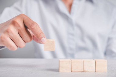 Mavi gömlekli bir iş adamı, boş tahta blokları elleriyle düzenliyor. Beyaz ahşap bir masanın üzerine yerleştirilmiş. İş stratejisi ve eylem planı. Boşluğu kopyala.